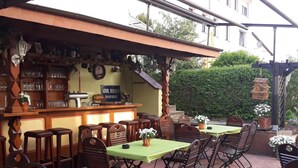 An outdoor patio with wooden tables and chairs, a bar area with shelves of glasses, and a green tablecloth-covered table. - Zwehrener Hof (Kassel)