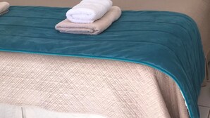 A neatly made bed with a teal bedspread, two teal pillows, and a folded white towel. - Antaira Bed and Tours (San Pedro de Atacama)