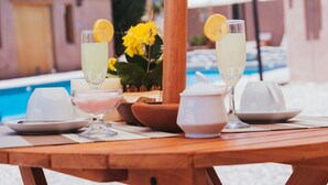 A table set with glasses of a light-colored beverage, a pitcher, and a bowl, with a pool and umbrellas in the background. - Antaira Bed and Tours (San Pedro de Atacama)