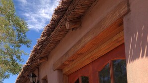 A rustic building with a thatched roof, a wooden door with glass panels, and a brick wall. - Antaira Bed and Tours (San Pedro de Atacama)