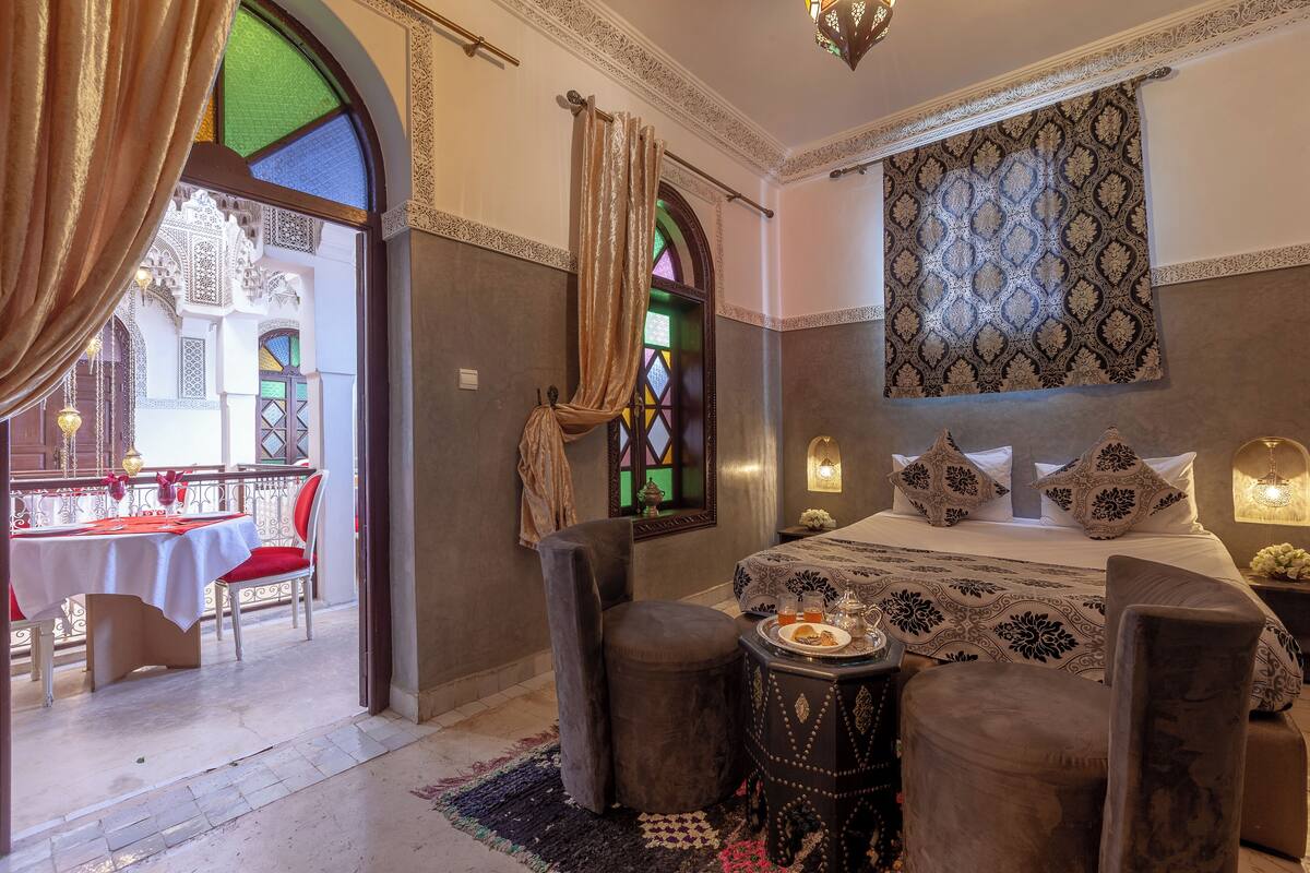 Une chambre d’hôtel avec un lit, une table et une chaise. Il y a un balcon avec une table et des chaises à l’extérieur.