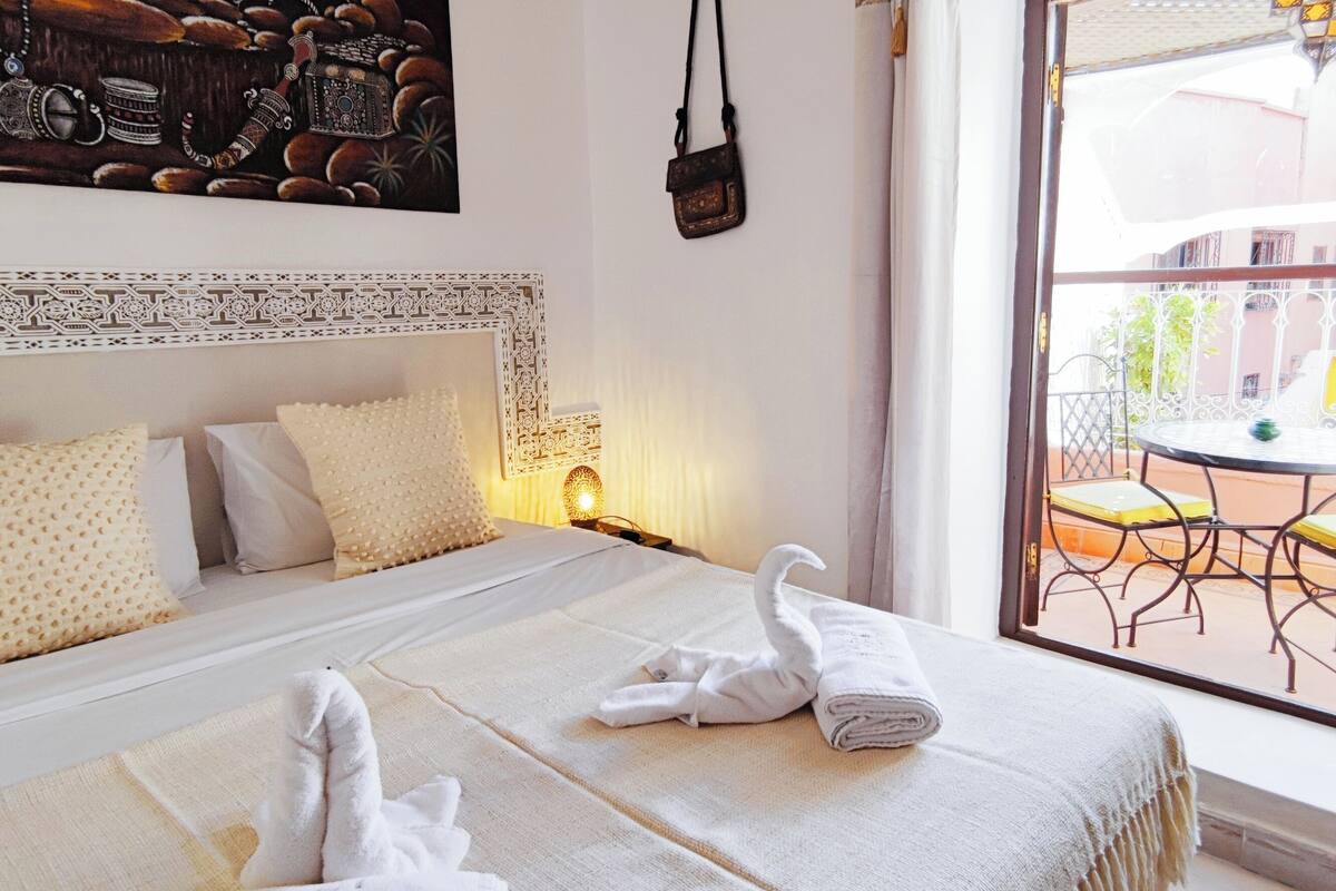 Une chambre d’hôtel avec un lit, des oreillers, une table de chevet, une lampe et une vue sur le balcon extérieur.