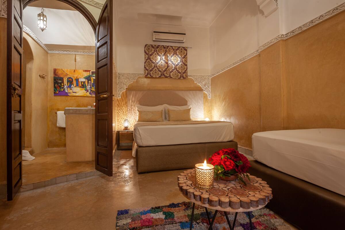 Une chambre d’hôtel avec un lit, une table de chevet ornée d’une bougie et de roses, une salle de bain avec une douche et un tableau accroché au mur.
