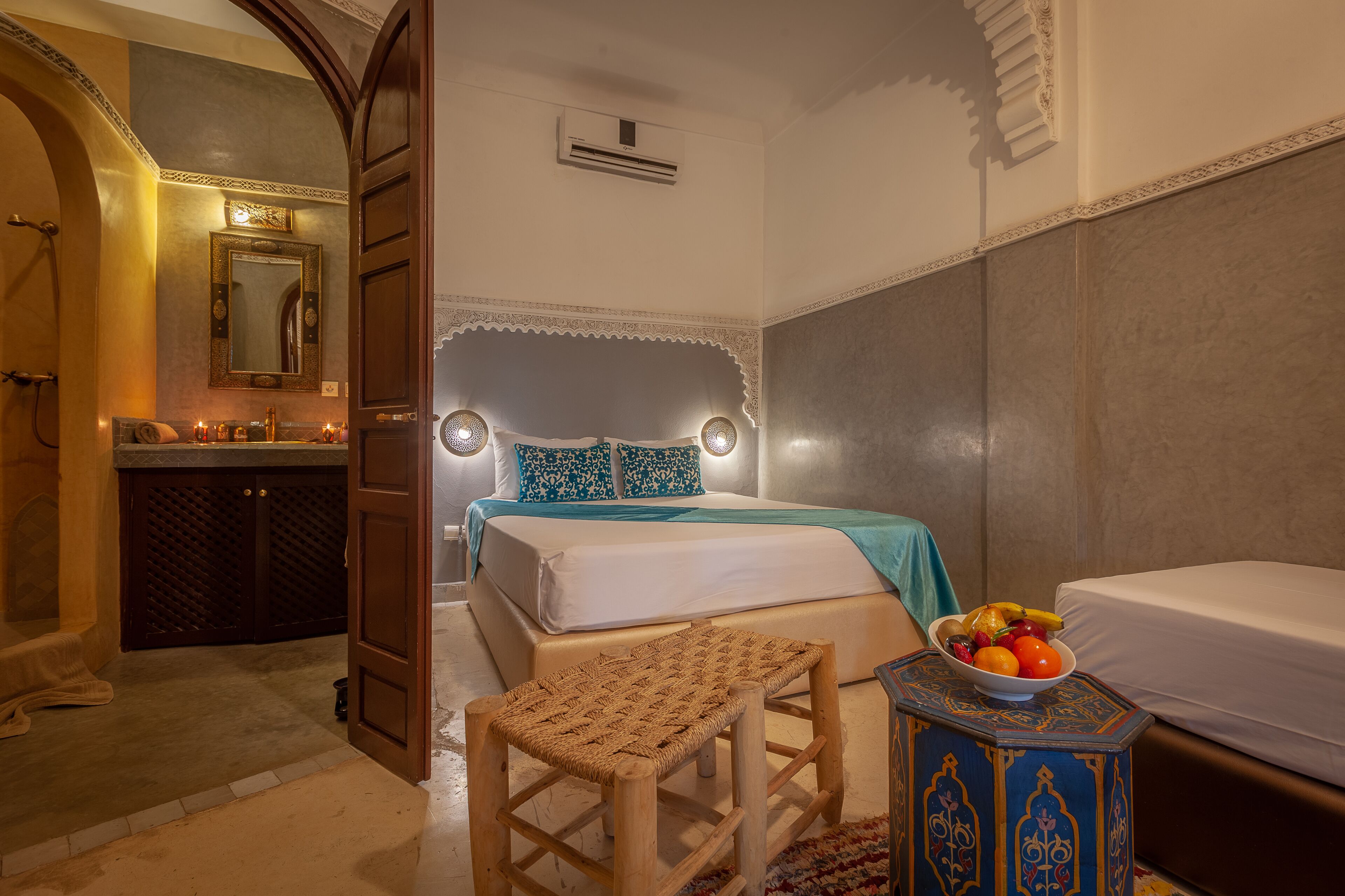 Un dormitorio con cama, mesita de noche y un taburete pequeño. Hay un cuenco con fruta sobre la mesita de noche.