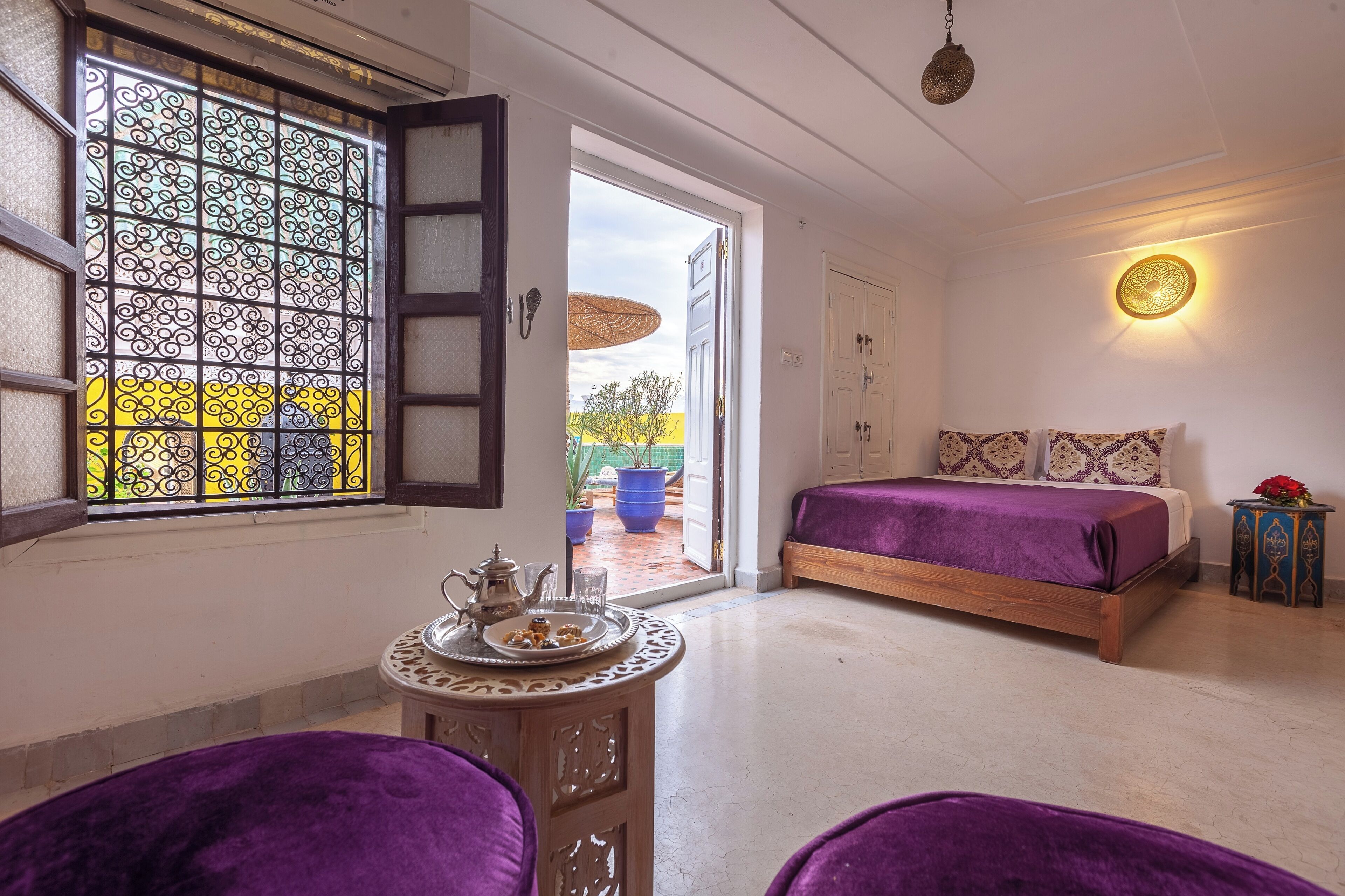 A bedroom with a bed, a table with a tray, a window with decorative glass, and a door leading outside.