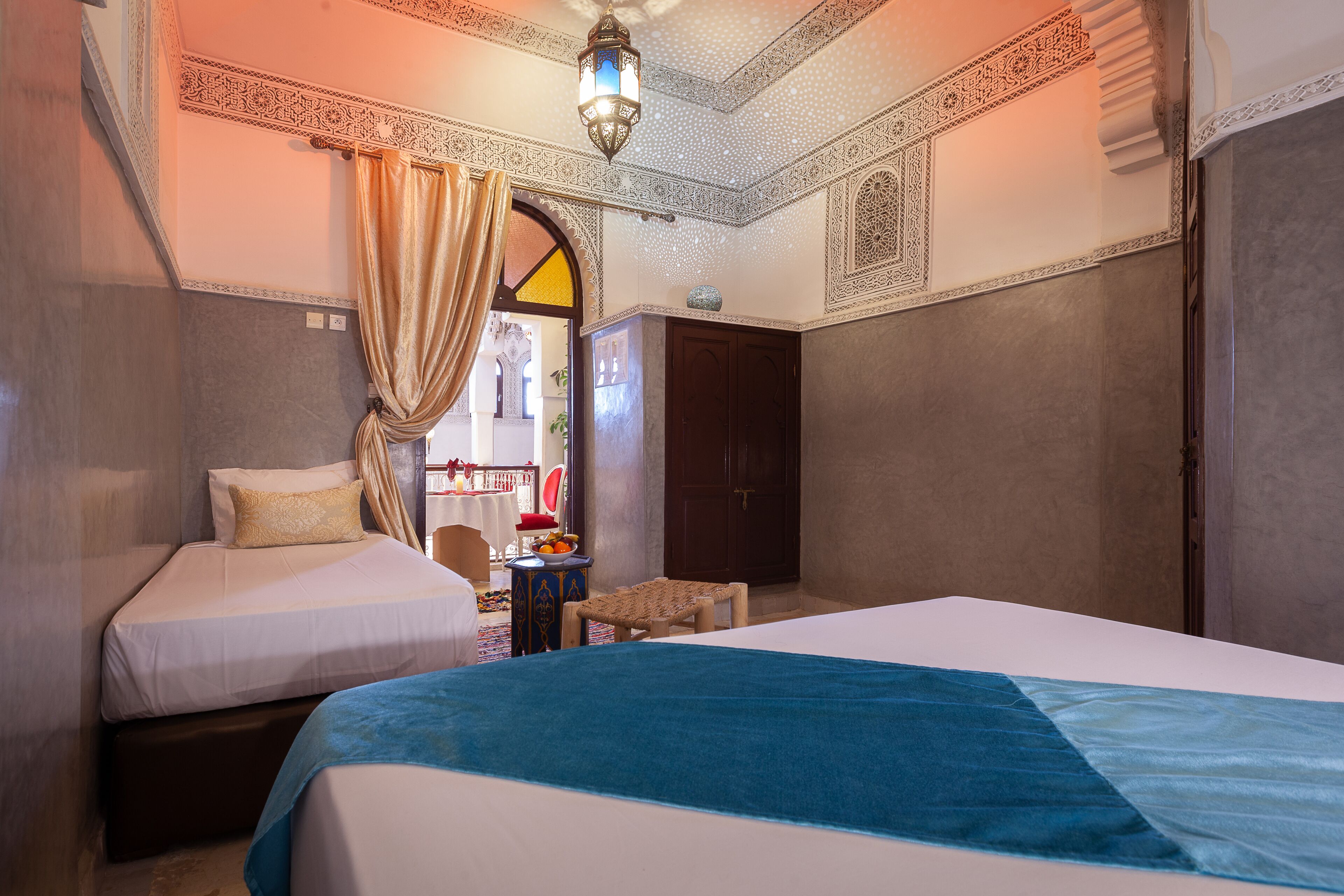 Habitación de hotel con dos camas, una mesita y un techo decorativo.