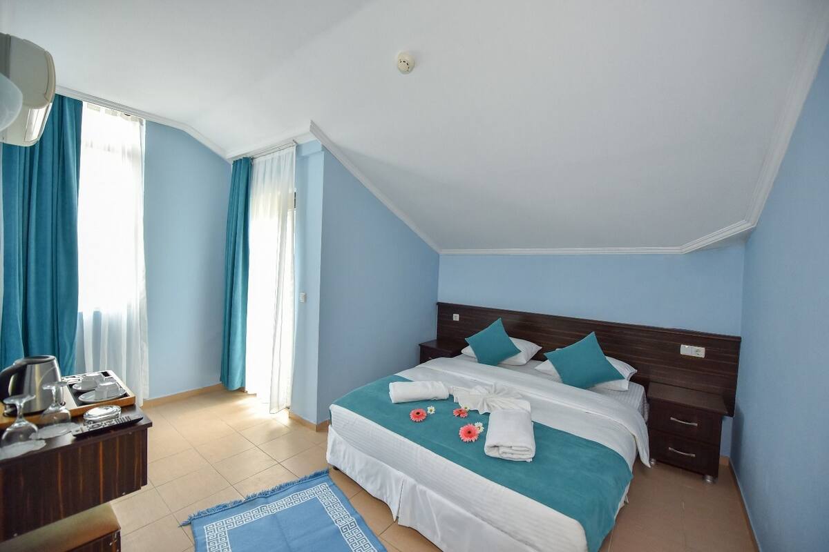 A bedroom with a bed, bedside tables, a desk with a coffee maker, and a window with curtains.