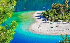 Une plage à l’eau turquoise et limpide, avec un rivage sablonneux et quelques zones verdoyantes.
