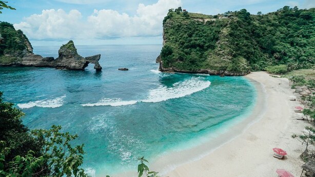 A beach with clear turquoise waters, a rocky outcrop, and lush greenery. - Gati Cottage (Penida Island)