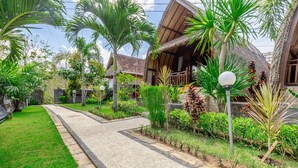 A pathway leading to a traditional-style building with a thatched roof, surrounded by lush greenery and small plants. - Gati Cottage (Penida Island)