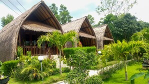 A bungalow with thatched roofs, surrounded by lush greenery and a well-maintained garden. - Gati Cottage (Penida Island)