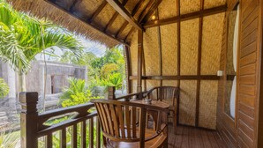 A wooden deck with a thatched roof, wooden chairs, and a view of tropical vegetation. - Gati Cottage (Penida Island)