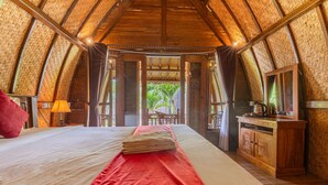 A room with a bed, a red blanket, a wooden cabinet, and a view of greenery outside. - Gati Cottage (Penida Island)