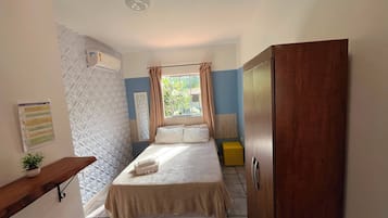 Un dormitorio con cama, una mesita de noche con planta, armario y ventana con cortinas.