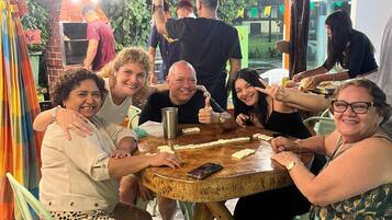 Un grupo de personas sentadas alrededor de una mesa redonda de madera, bajo un paraguas rojo, jugando.