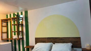 Un dormitorio con cama, cabecera de madera, mesita de noche, estante con toallas y pared con estampado a rayas verdes y blancas.