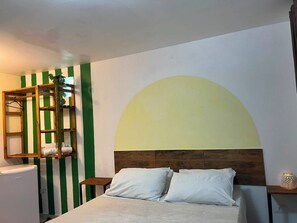 Une chambre à coucher comprenant un lit, une tête de lit en bois, une table de chevet, une étagère avec des serviettes et un mur orné d’un motif à rayures vertes et blanches.