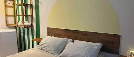 A bedroom with a bed, a nightstand, a wall-mounted shelf, and a radiator.