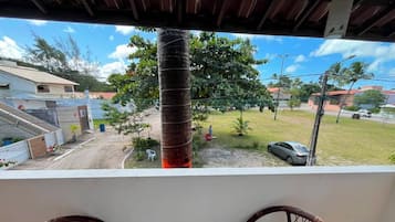 Un balcón con sillas de mimbre, vista a un árbol y un coche estacionado.