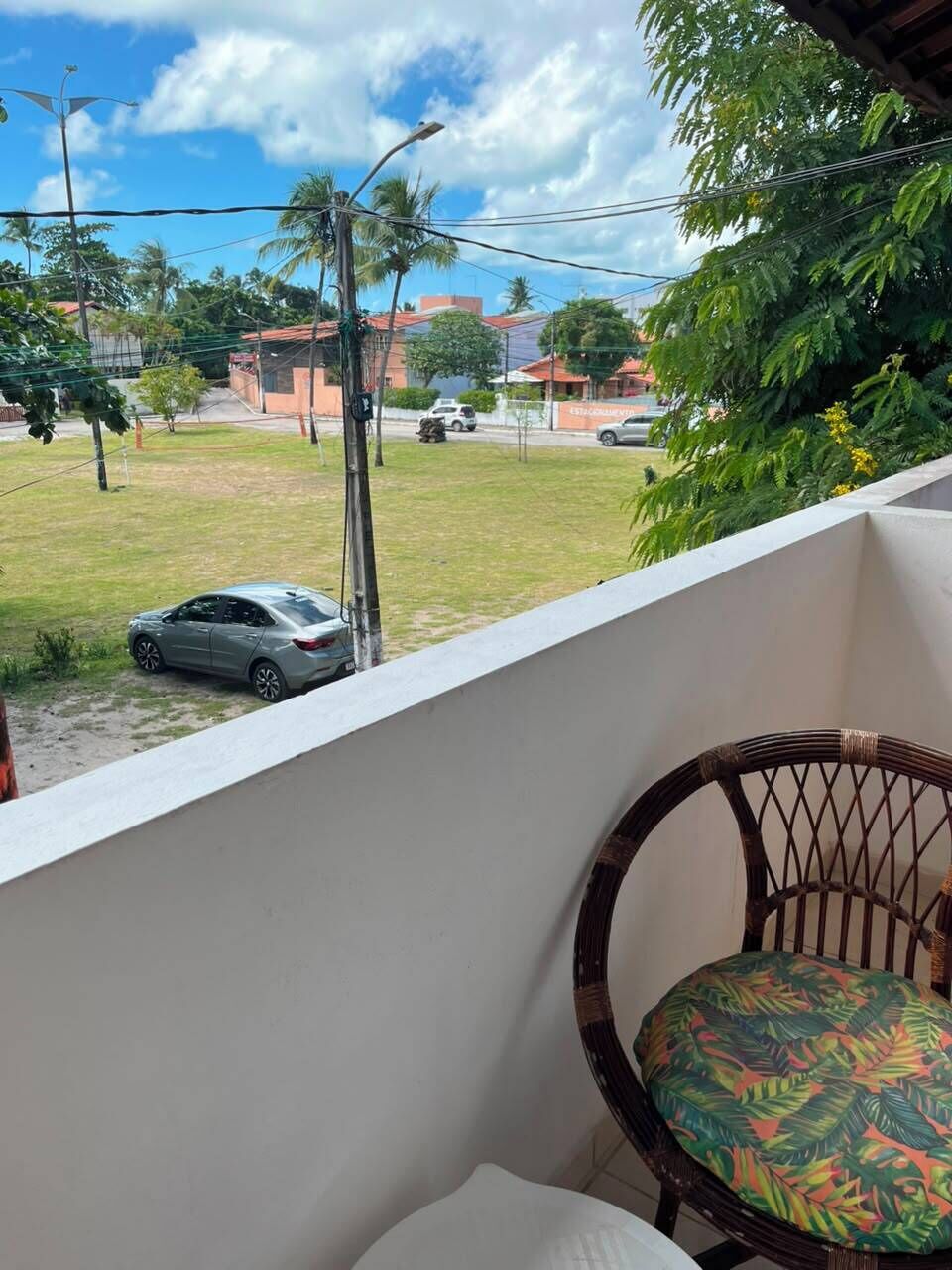 A balcony with a view of a street, a parked car, and a chair with a patterned cushion.