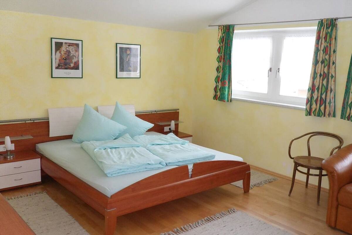 A bedroom with a bed, a nightstand, a chair, and a window with curtains.