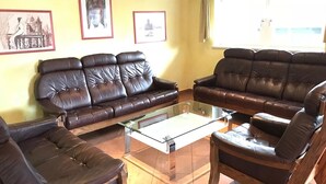 A living room with two brown leather sofas, a glass coffee table, and a wooden armchair. - Appartementhaus Holiday & Villa Theresa (Kaprun)