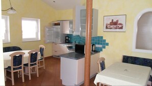 A compact kitchen with white cabinets, a built-in microwave, and a coffee maker. There is a dining table with chairs and a window providing natural light. - Appartementhaus Holiday & Villa Theresa (Kaprun)