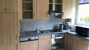 A kitchen with wooden cabinets, a stainless steel range, a double sink, and a window with a view of greenery. - Appartementhaus Holiday & Villa Theresa (Kaprun)