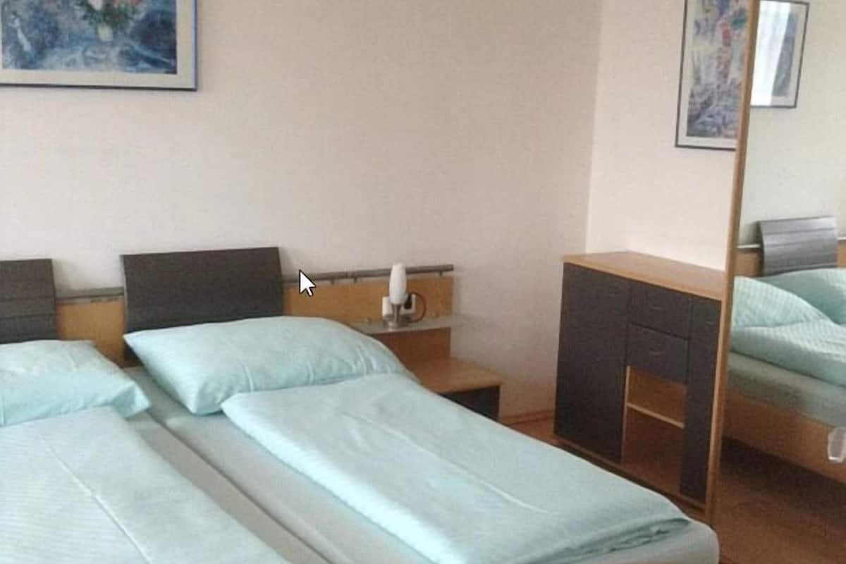 A room with two single beds, a wooden desk, a chair, a mirror, and a framed picture on the wall.