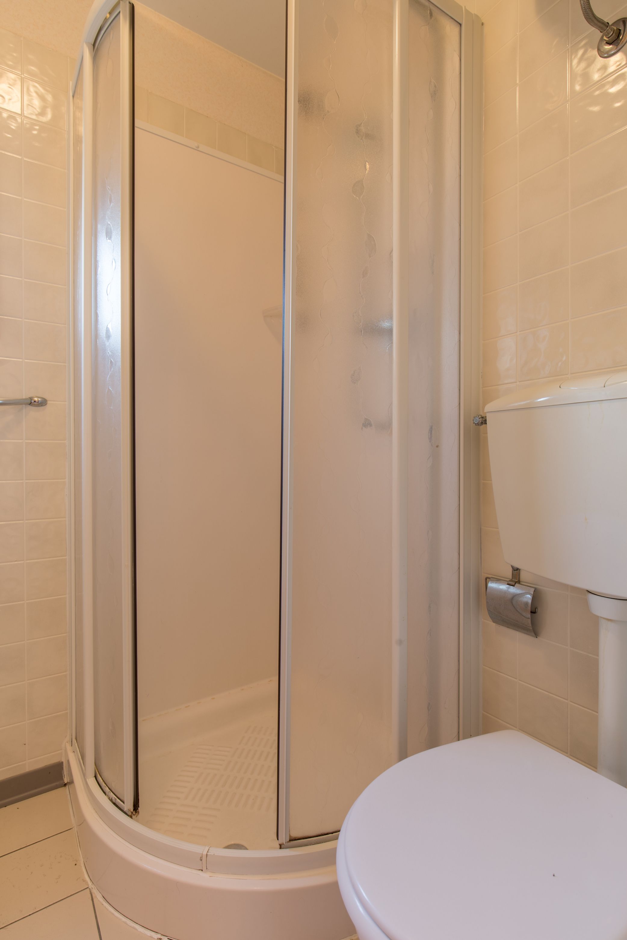 A bathroom with a glass-enclosed shower, a toilet, and tiled walls.