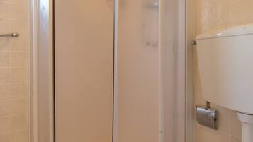 A bathroom with a glass-enclosed shower, a toilet, and tiled walls.