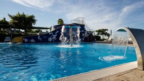 A swimming pool with water jets and a slide, surrounded by lounge chairs and a covered area. - Camping Sun Beach (Torino di Sangro)