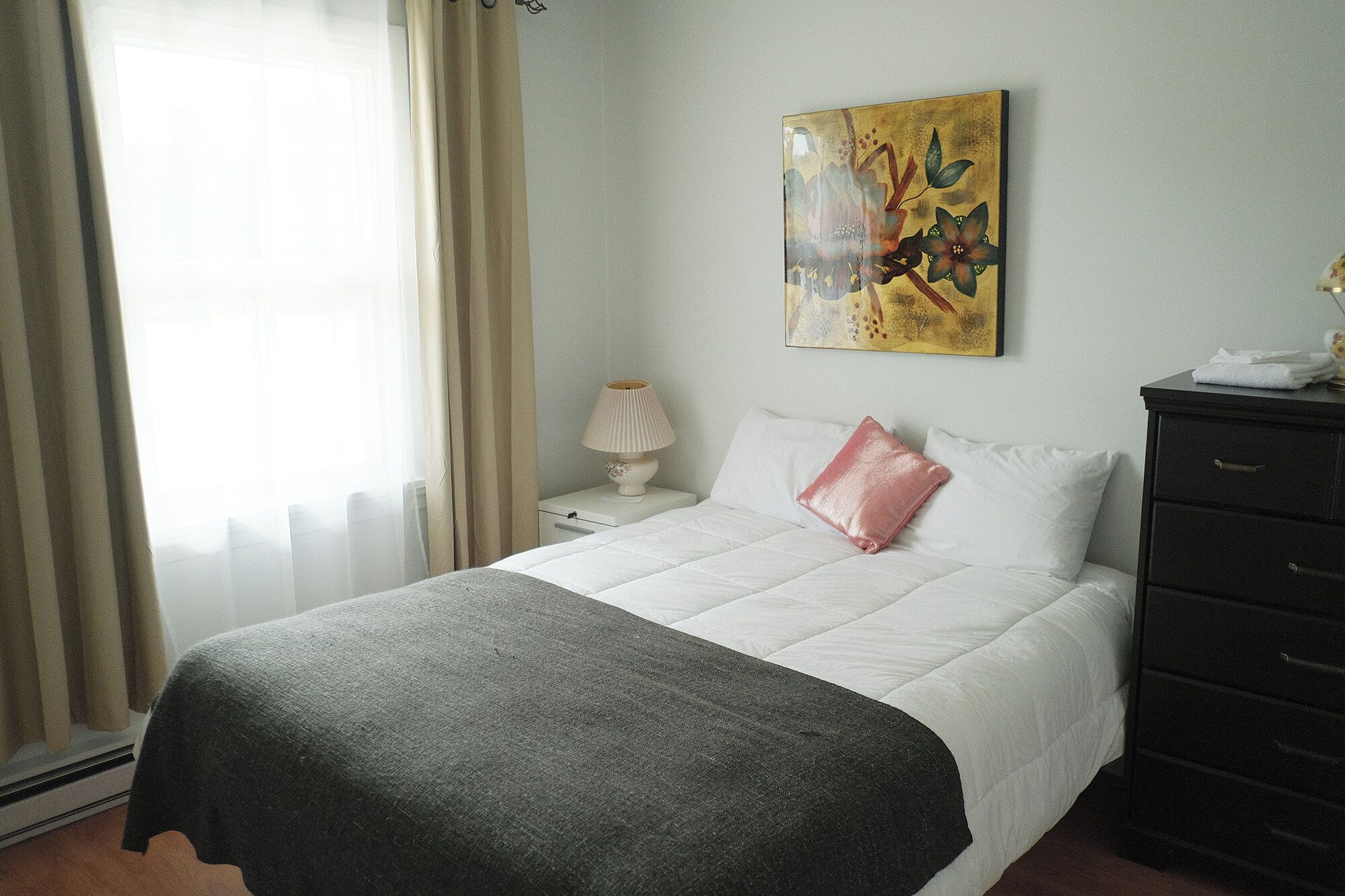 Una habitación de hotel con cama, mesita de noche, lámpara, cómoda y un cuadro en la pared.