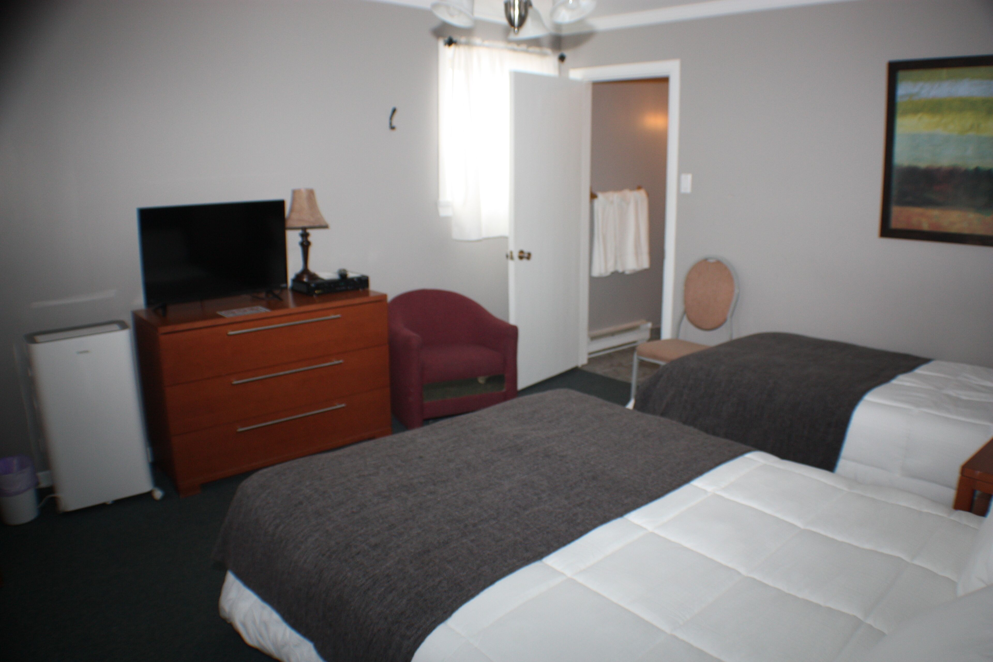 Habitación de hotel con cama, escritorio con televisor, una silla y un refrigerador pequeño.