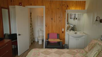 A bedroom with a bed, a desk, a chair, a small bathroom with a toilet, and a sink.