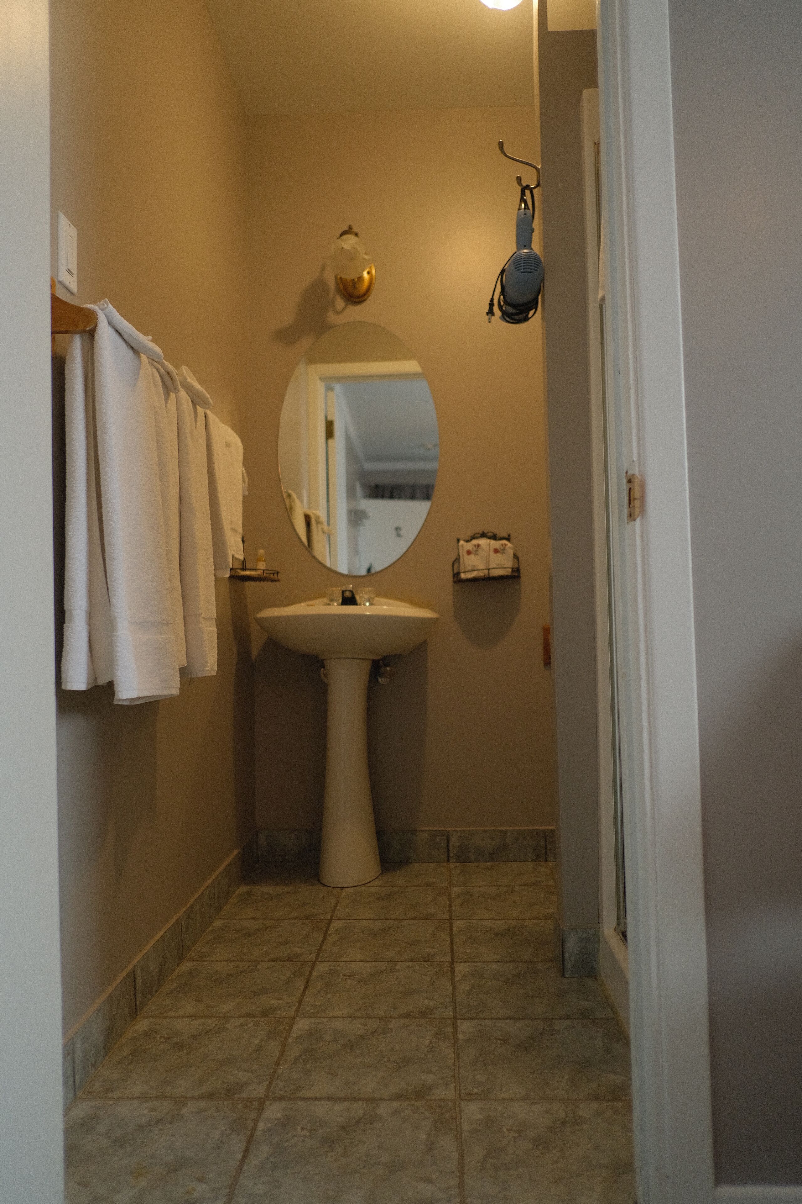 A narrow bathroom with a pedestal sink, a wall-mounted mirror, and a towel rack with multiple towels.