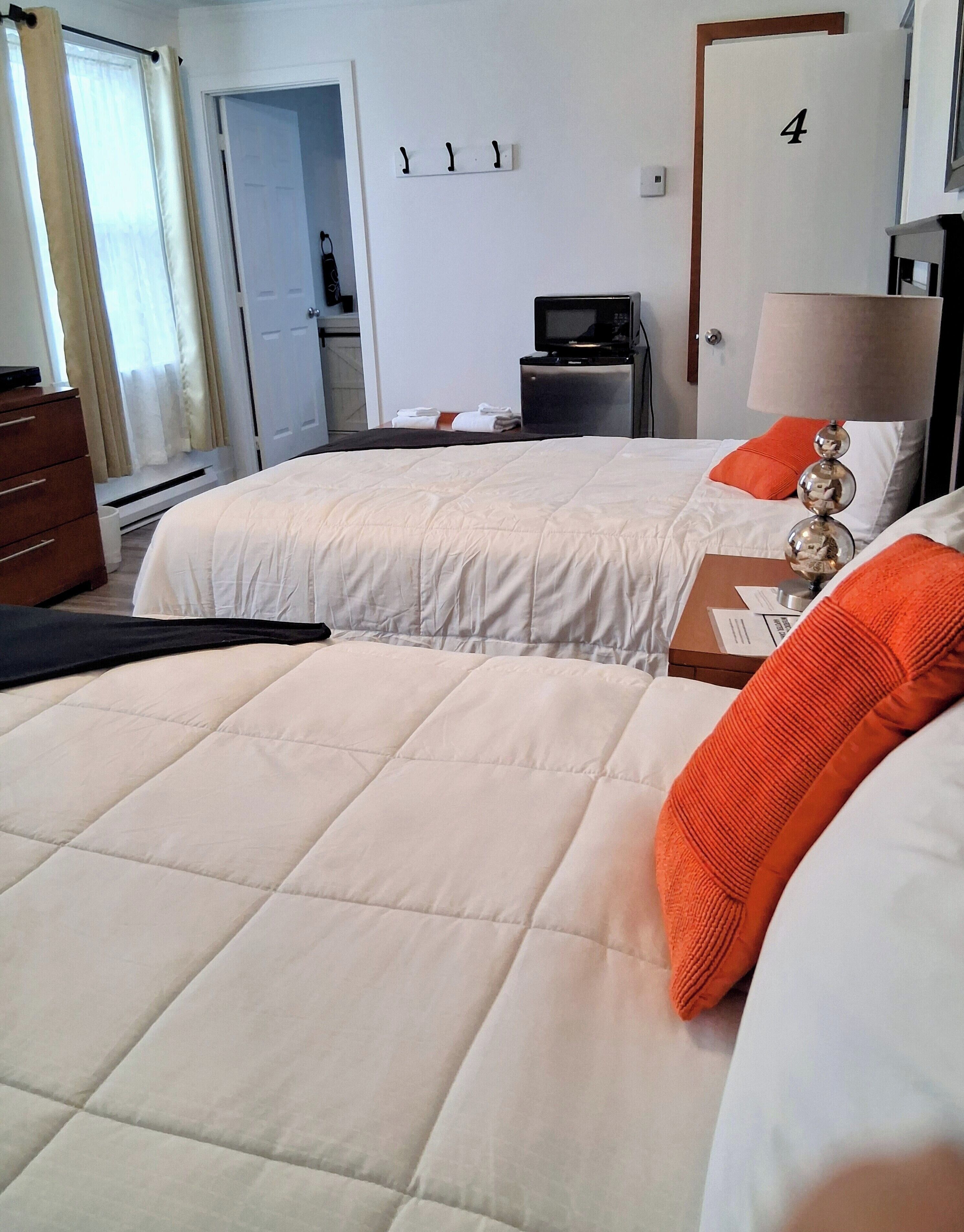 A hotel room with two beds, a desk, a TV, and a lamp.
