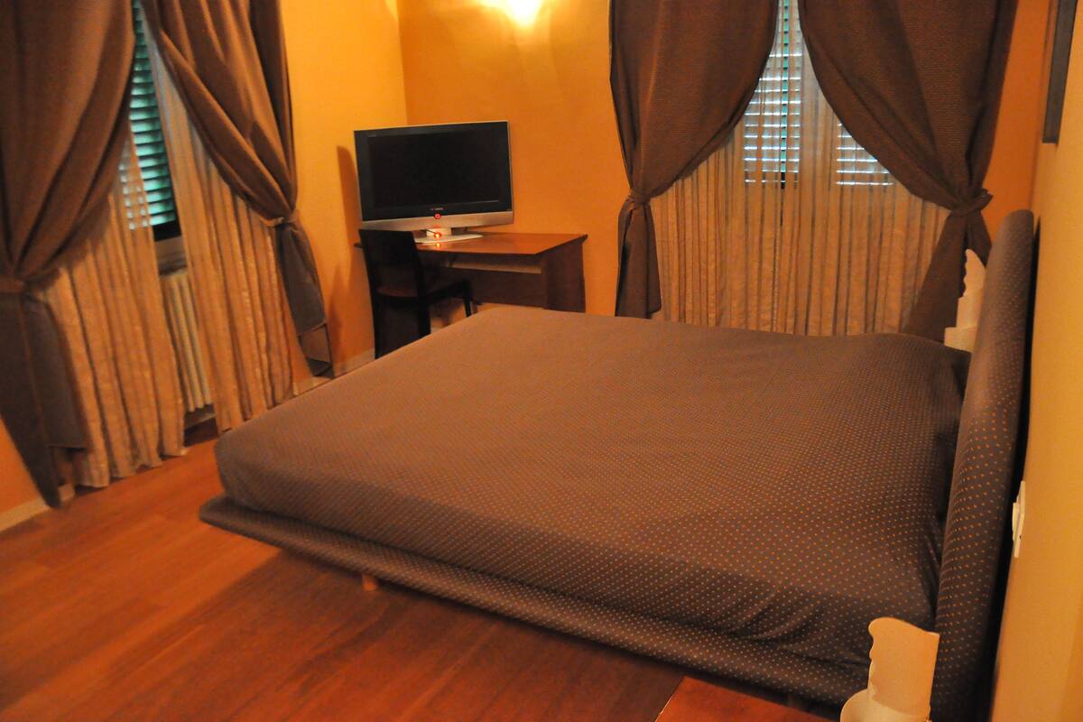 Een slaapkamer met een groot bed, een bureau en een flatscreen-tv, en gordijnen.