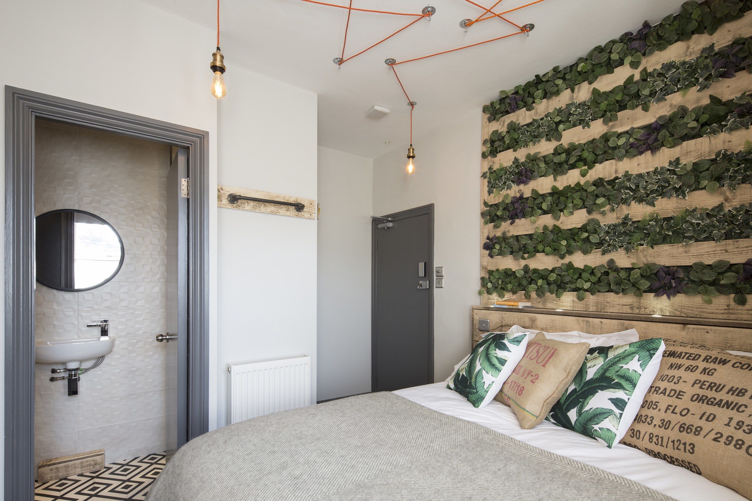 Une chambre à coucher avec un lit, un mur végétal, un miroir rond et une table de chevet.