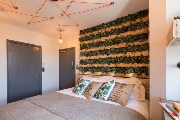 A bedroom with a bed, a wooden wall with greenery, a door, and a ceiling light fixture.