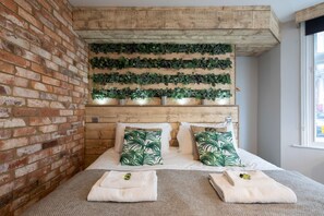 Ein Zimmer mit Backsteinwand, Holzboden und einem Bett mit grün gemusterten Kissen.