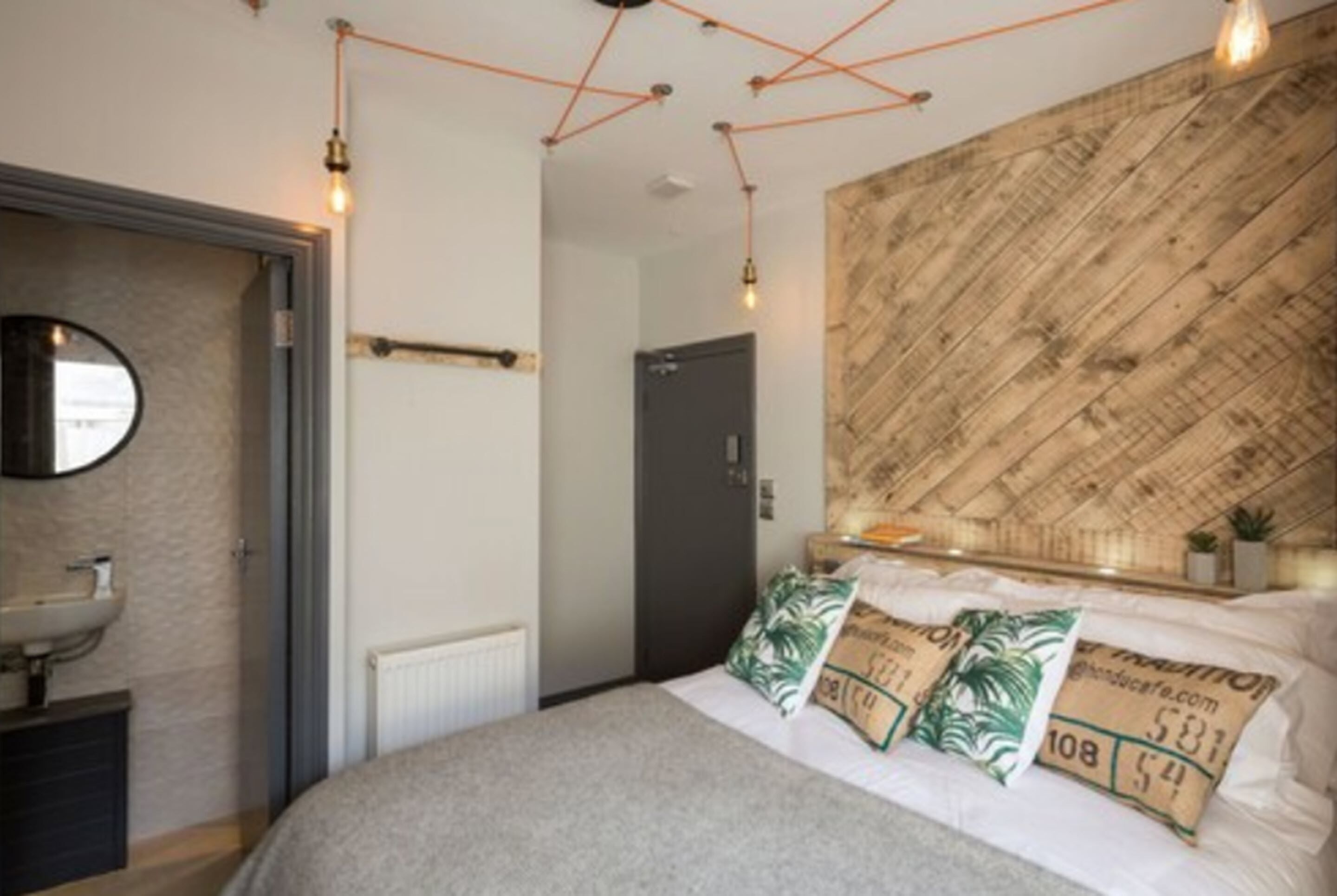 A bedroom with a bed, a wooden headboard, a round mirror, and a bedside table with a lamp.