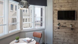 Una habitación con una mesa redonda de madera, una computadora portátil, una planta en maceta, una silla, un radiador y un televisor montado en una pared de madera.