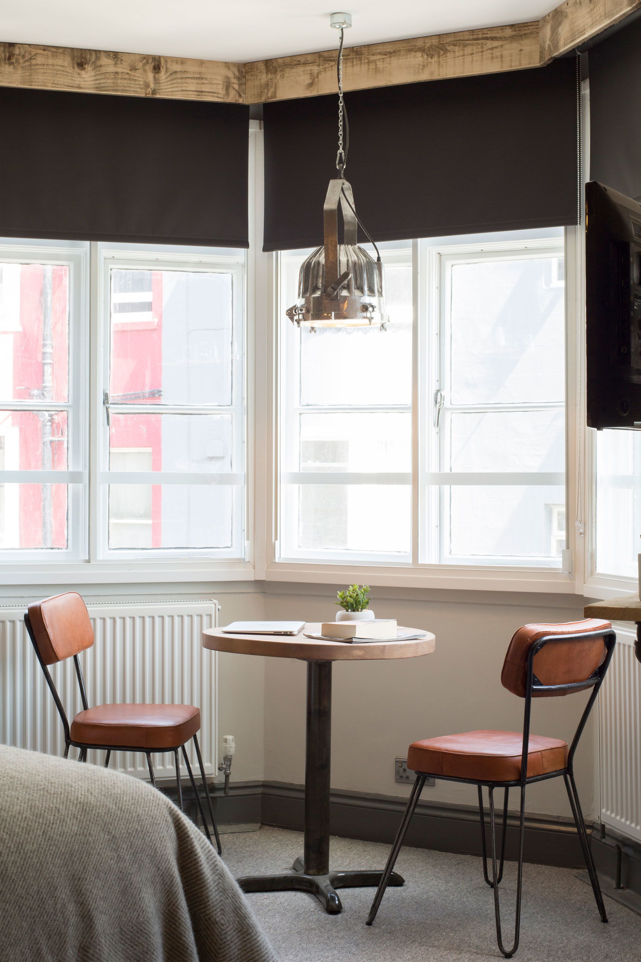 Et værelse med et rundt bord, to stole, en hængende lampe og et stort vindue med persienner.