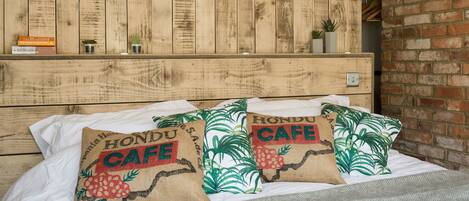A bed with two pillows labeled "Hondou Cafe" and a wooden headboard with a shelf above it.