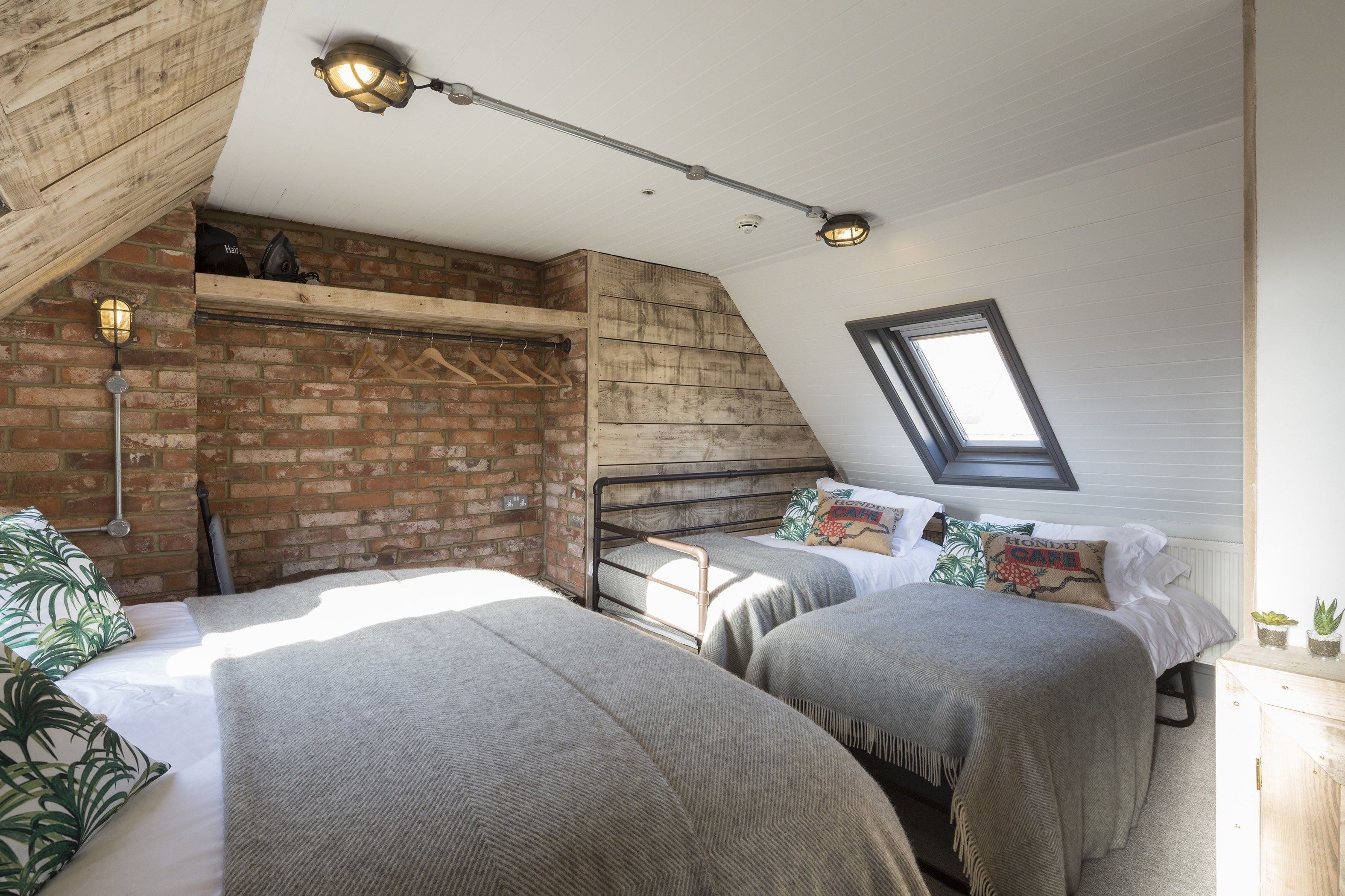 A loft bedroom with two beds, a skylight, and exposed brick walls.
