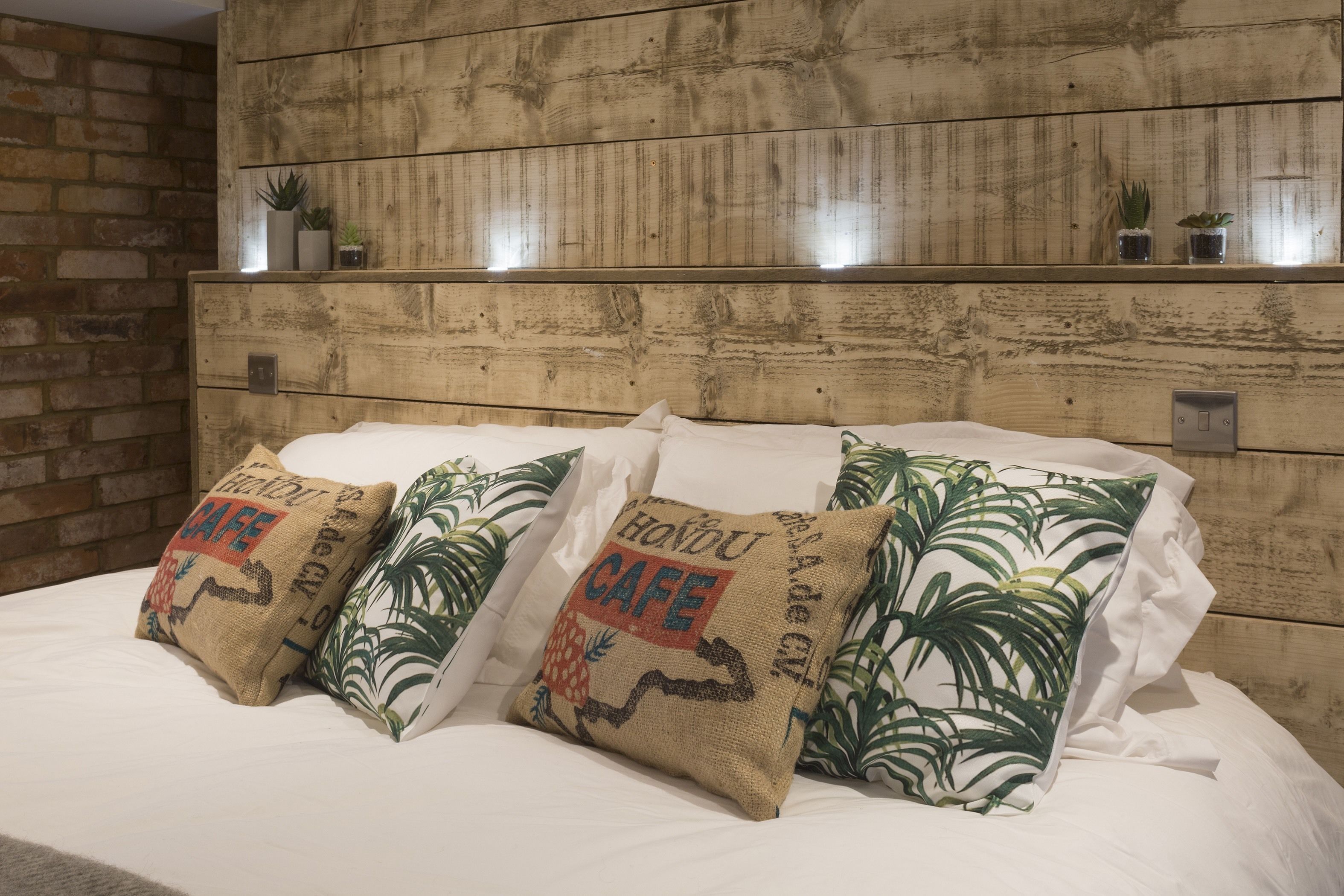 Ein Bett mit weißer Bettwäsche und drei Kissen, eines mit Jutetextur und die anderen mit einem grünen Blattmuster.