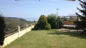 A grassy outdoor area with a wooden fence, a bench, and a view of the sea. - Villa Eva Agios Nikolaos (Sithonia)