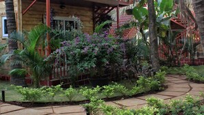 A wooden house with a balcony, surrounded by lush greenery and a stone pathway. - Mariners Bay Resorts (Mandrem)