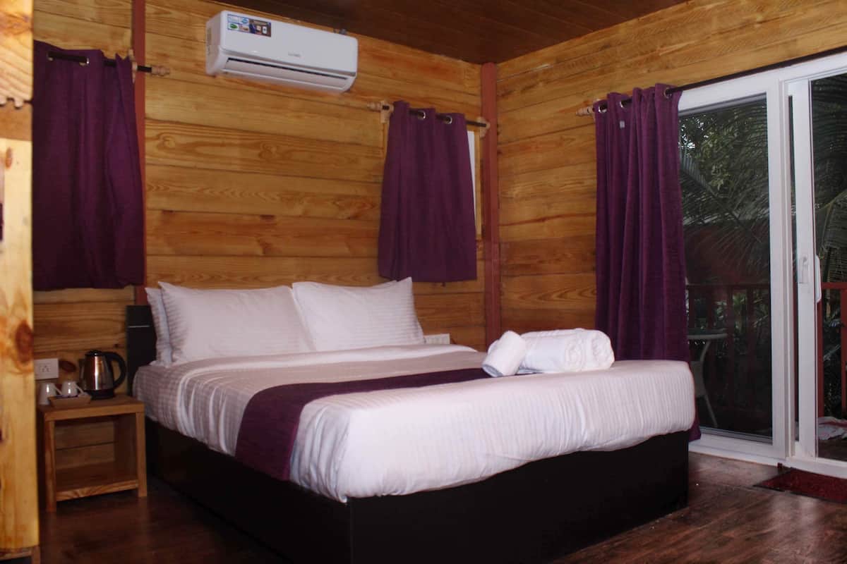 A wooden cabin bedroom with a bed, a nightstand, an air conditioning unit, and a sliding glass door to the outside.